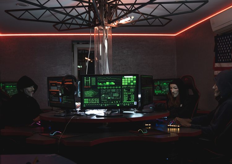 Hakerzy w maskach przy wielu monitorach symbolizujący cyberatak i wyciek danych z sieci Żabka